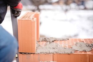 construction mason worker bricklayer installing brick walls with trowel putty knife outdoors during winter